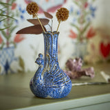 Kali Speckled Stoneware Vase 16cm in Blue, bird-shaped with a scalloped rim and carved feather details, shown with dried flowers on a shelf against patterned wallpaper.