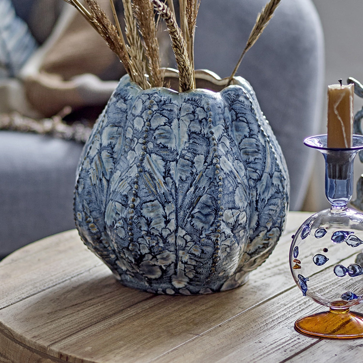 Hetty Stoneware Vase 19.5cm in blue, shown with ribbed, beaded texture and scalloped rim holding dried wheat stems on a wooden table beside a candle holder.
