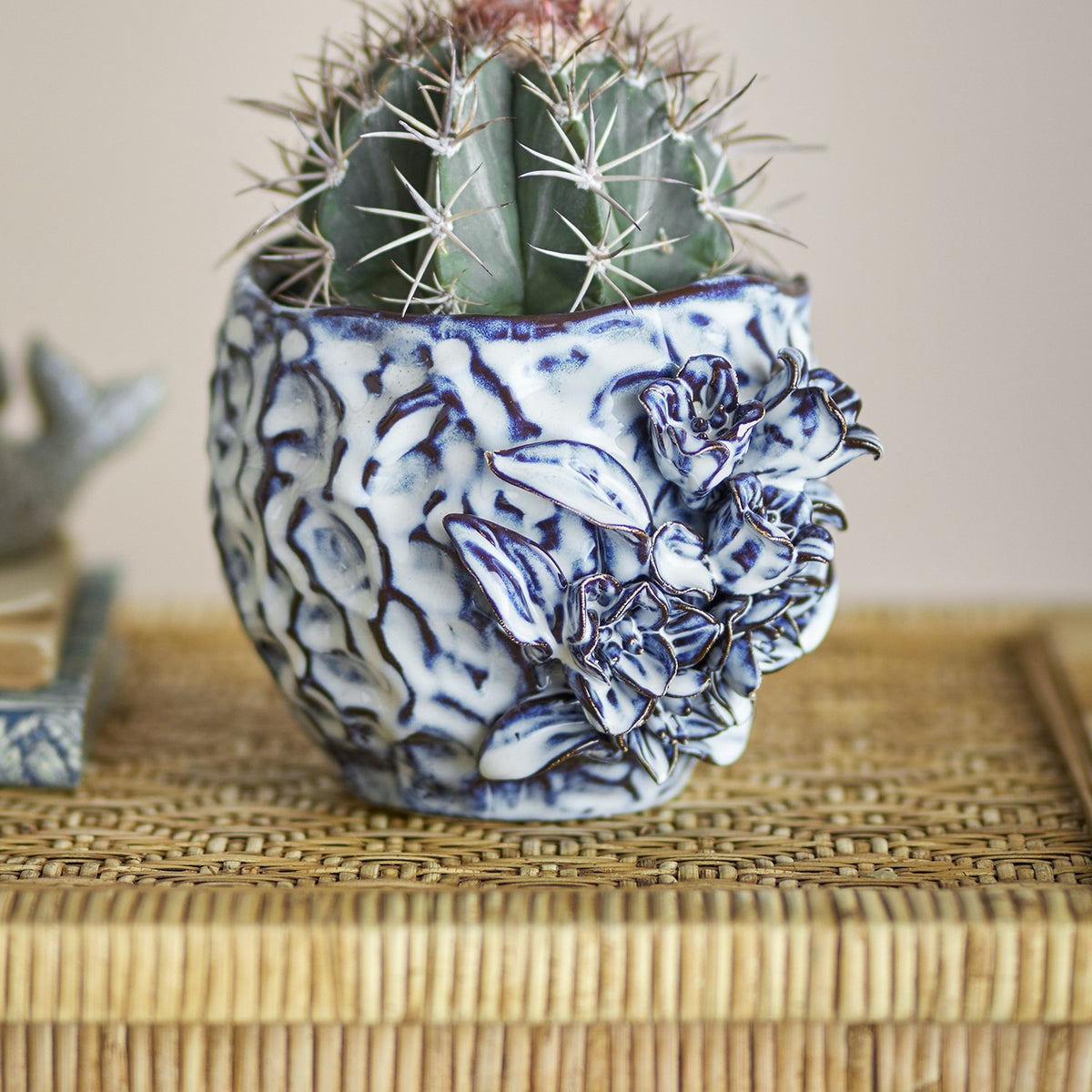 Malina Floral Stoneware Plant Pot in blue, ceramic with crinkled textured sides and raised floral relief, shown holding a cactus on a woven surface.
