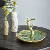 Litton Round Stoneware Tray in green, a leaf-shaped ceramic dish with ribbed, scalloped edges and a branch-like ring holder, shown with a beaded bracelet beside textured vases.