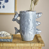 Tace Stoneware Vase 23cm in blue with three sculpted fish appearing to swim through its sides, shown with dried grasses on a woven side table.