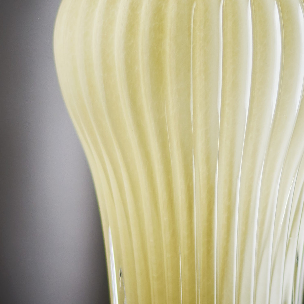 Close-up of the Averie 28cm mouth-blown glass vase in yellow, showing fine vertical ribs and softly translucent glass against a plain grey background.