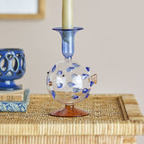 Phila Glass Candle Holder in Blue, a puffer fish-shaped glass candle holder with blue spine dots and flared blue cup, holding a taper candle on a woven side table.