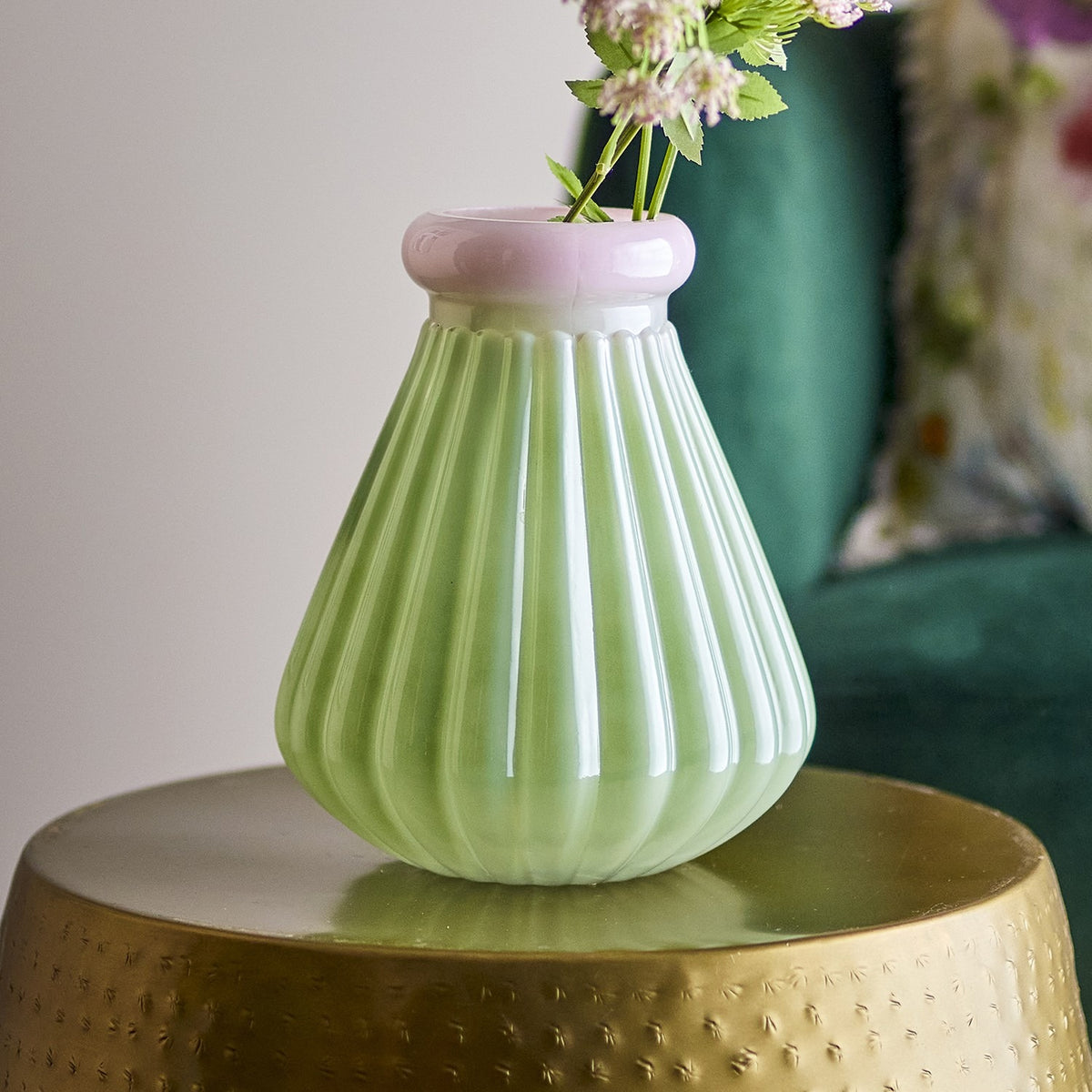 Judith Ribbed Glass Vase 24.5cm in green with a pink-rimmed neck, holding flowers on a gold side table beside a teal armchair.