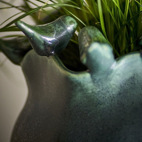 Close-up of the Charlize Stoneware Plant Pot in green, showing a reactive glazed finish and modelled bird details around the rim, with greenery visible behind.