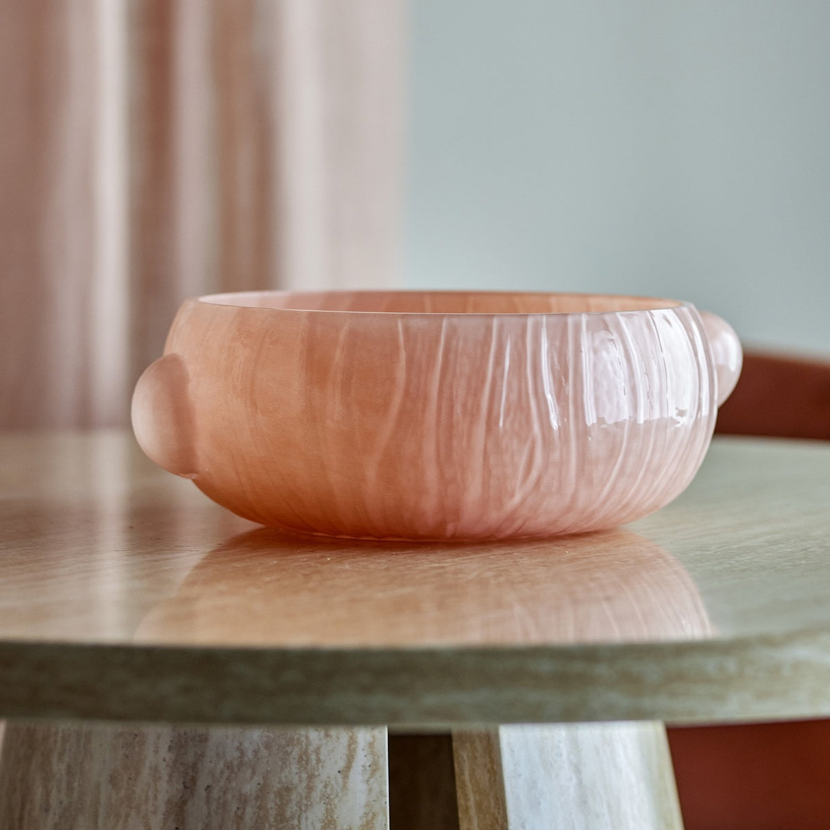 Lalie Ribbed Glass Bowl 20x12.5cm in pink, round with textured ribbed sides and two rounded side lugs, shown on a marble-topped table against a soft pink curtain backdrop.