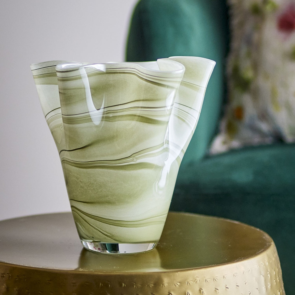 Toryn Marbled Glass Vase 24cm in green, mouthblown with a wavy folded rim and flared shape, shown on a gold side table against a green armchair.