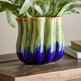Jenner Stoneware Plant Pot in Green, ribbed ceramic planter with scalloped rim and reactive glaze fading from green to deep blue, shown with foliage on a wooden table.