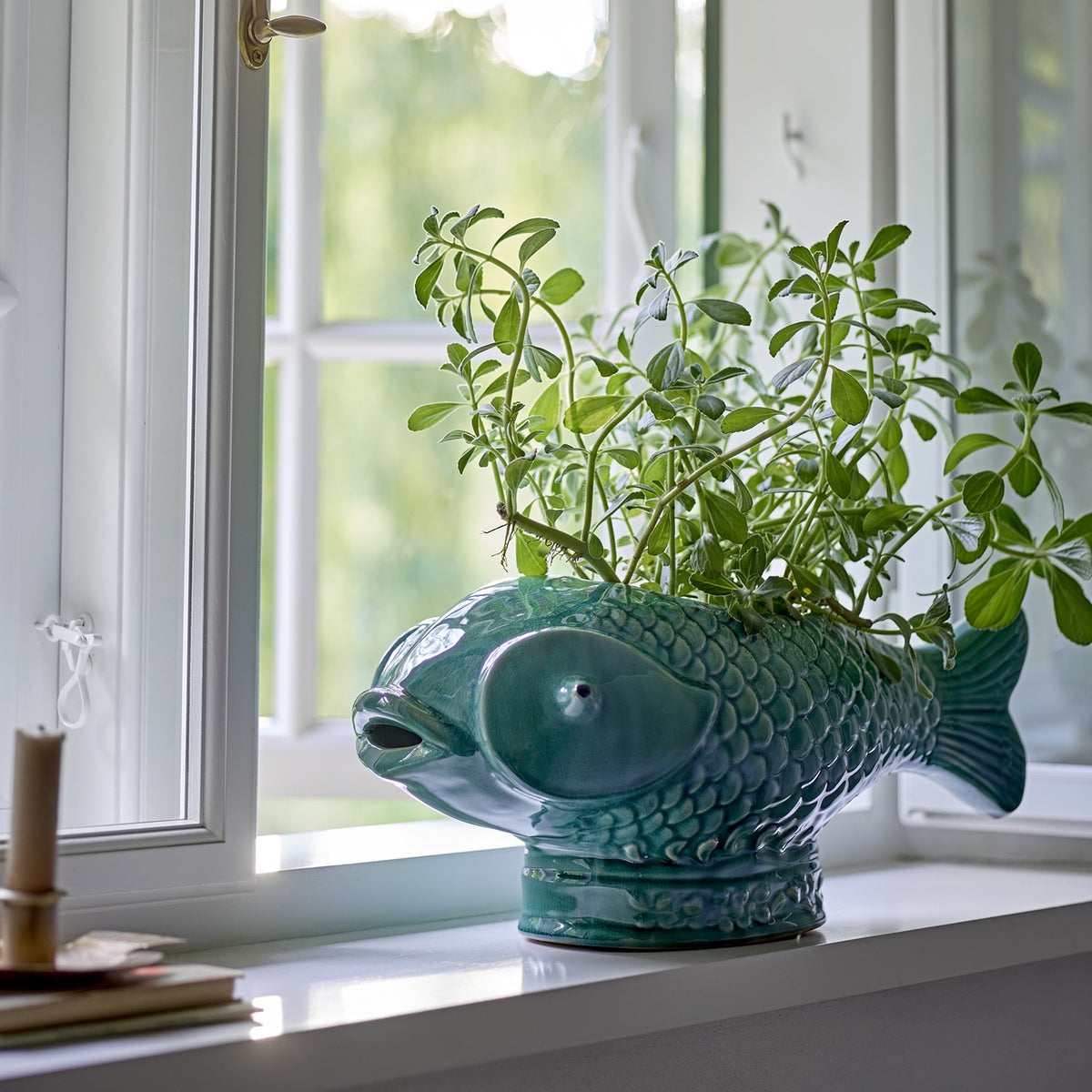 Hiro Fish Stoneware Plant Pot in green reactive glaze with raised scale detail, shown on a windowsill filled with trailing green foliage.