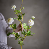 Chrysanthemum Artificial Stem 101cm in White, held by hand, showing layered white blooms and green leaves on a branching stem against a neutral background.