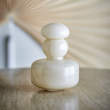 Cynthia Glass Vase 21cm in Beige, a glossy mouth-blown glass vase with a stacked design of a broad base, ball-shaped neck and mushroom-domed stopper, shown on a reflective tabletop.