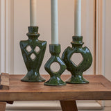 Weio Geometric Stoneware Candle Holders Set of 3 in green, with diamond and circle cut-outs in varying heights, holding white taper candles on a wooden table.
