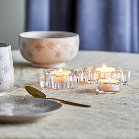 Dania Snowflake Glass Christmas Tealight Holders, set of 3 clear glass snowflake-shaped candle holders with lit tealights, styled on a table with bowls and a spoon.