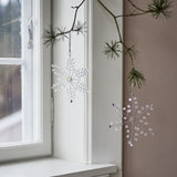 Miku Snowflake Christmas Tree Decorations, Set of 2, clear beaded wire snowflakes hanging from a pine branch beside a white-framed window.