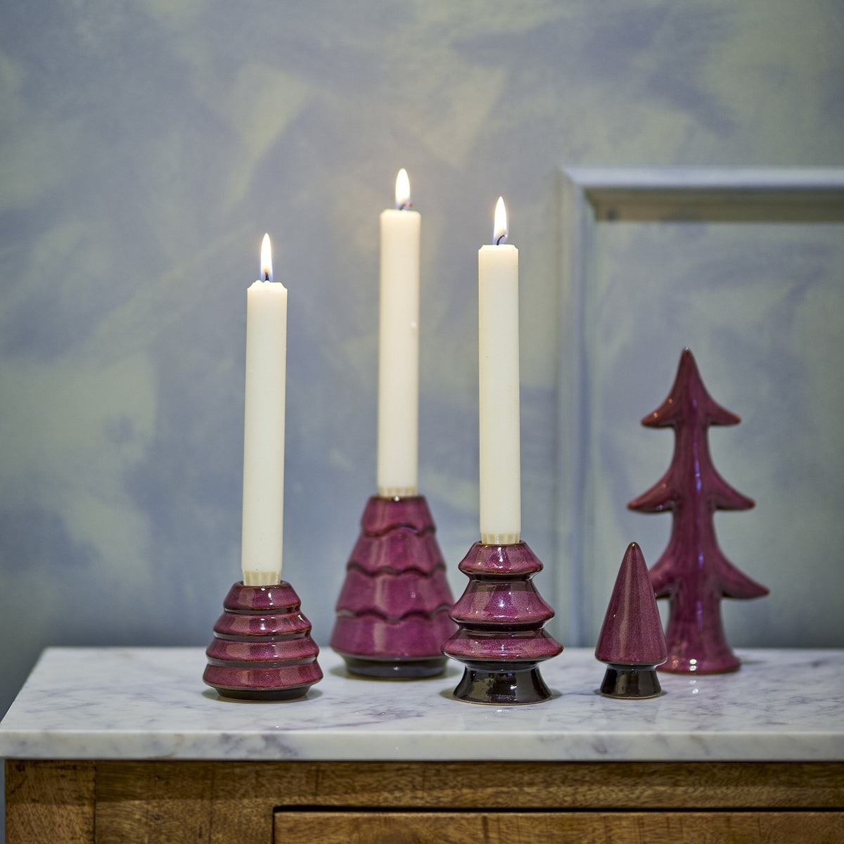 Woods Stoneware Christmas Candle Holders Set of 5 in purple, three tree-shaped holders with lit taper candles beside two matching tree ornaments on a marble surface.