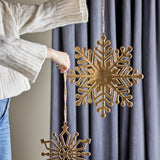 Kanja gold iron snowflake Christmas tree decorations, set of 2 in different sizes, held by cord against a grey curtain backdrop.