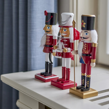 Darren Wooden Christmas Decorations set of 3 nutcracker-style soldier figures in red, white and gold, with sabre, drum and flag pole details, displayed on a white table.