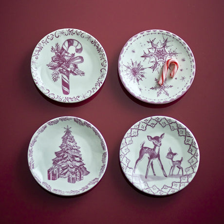 Set of four small stoneware Christmas plates in pink on white, each with a different design: candy cane with ribbon, snowflakes, decorated tree with presents, and deer in a lattice border.