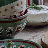 Peo Stoneware Christmas Bowls, 13cm, stacked with green exterior and cream interior featuring angel mice motifs, shown beside a matching plate, rosemary sprig, and cheese on a wooden table.