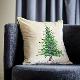 Evelin Cotton Christmas Cushion in cream with a painted green Christmas tree design, green piped edge, shown on a dark grey sofa against striped curtains.
