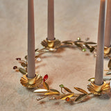 Gold iron Advent candle holder wreath with four flower-shaped cups holding taupe candles, accented by leaf sprigs and coloured faceted berry details.