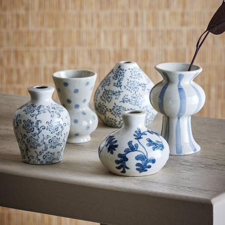 Quinto Striped Stoneware Vases Set of 5 in blue, five small ceramic vases with floral, dotted, leafy and striped patterns, on a wooden surface against a woven backdrop.