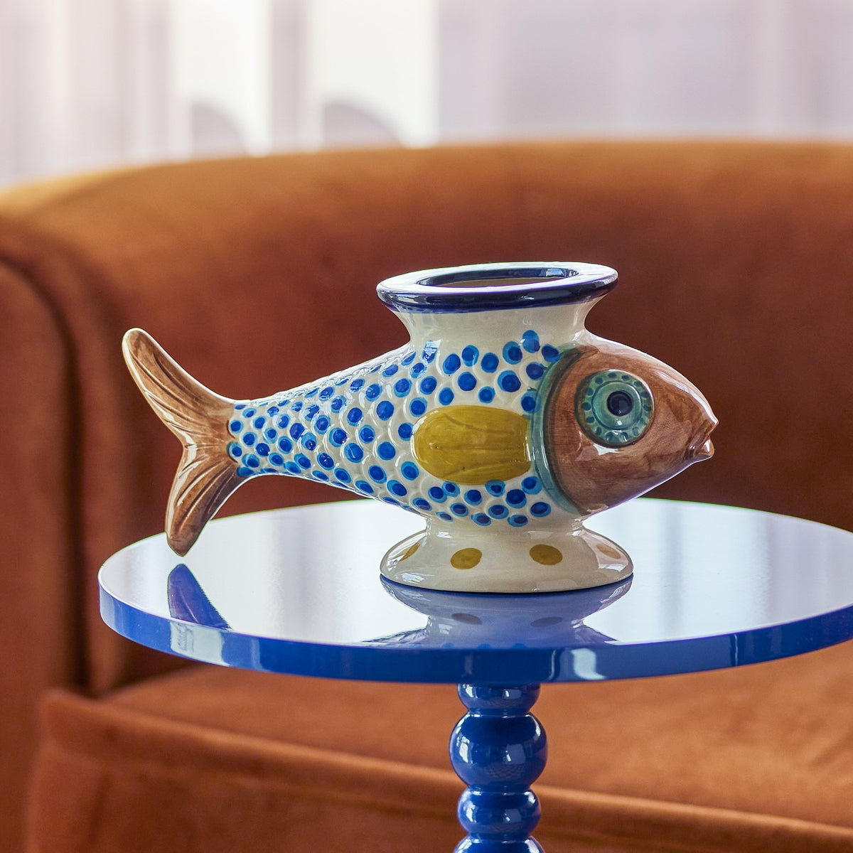 Nobu Fish Stoneware Vase 15cm in multicoloured hand-painted ceramic with scale-dot pattern and flared rim, displayed on a blue side table against a rust-coloured armchair.
