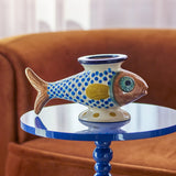 Nobu Fish Stoneware Vase 15cm in multicoloured hand-painted ceramic with scale-dot pattern and flared rim, displayed on a blue side table against a rust-coloured armchair.