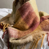 Hamisha Throw - Multi, a large checked woven throw in pink, gold, and green tones with a chunky twisted fringe, draped over a bed.