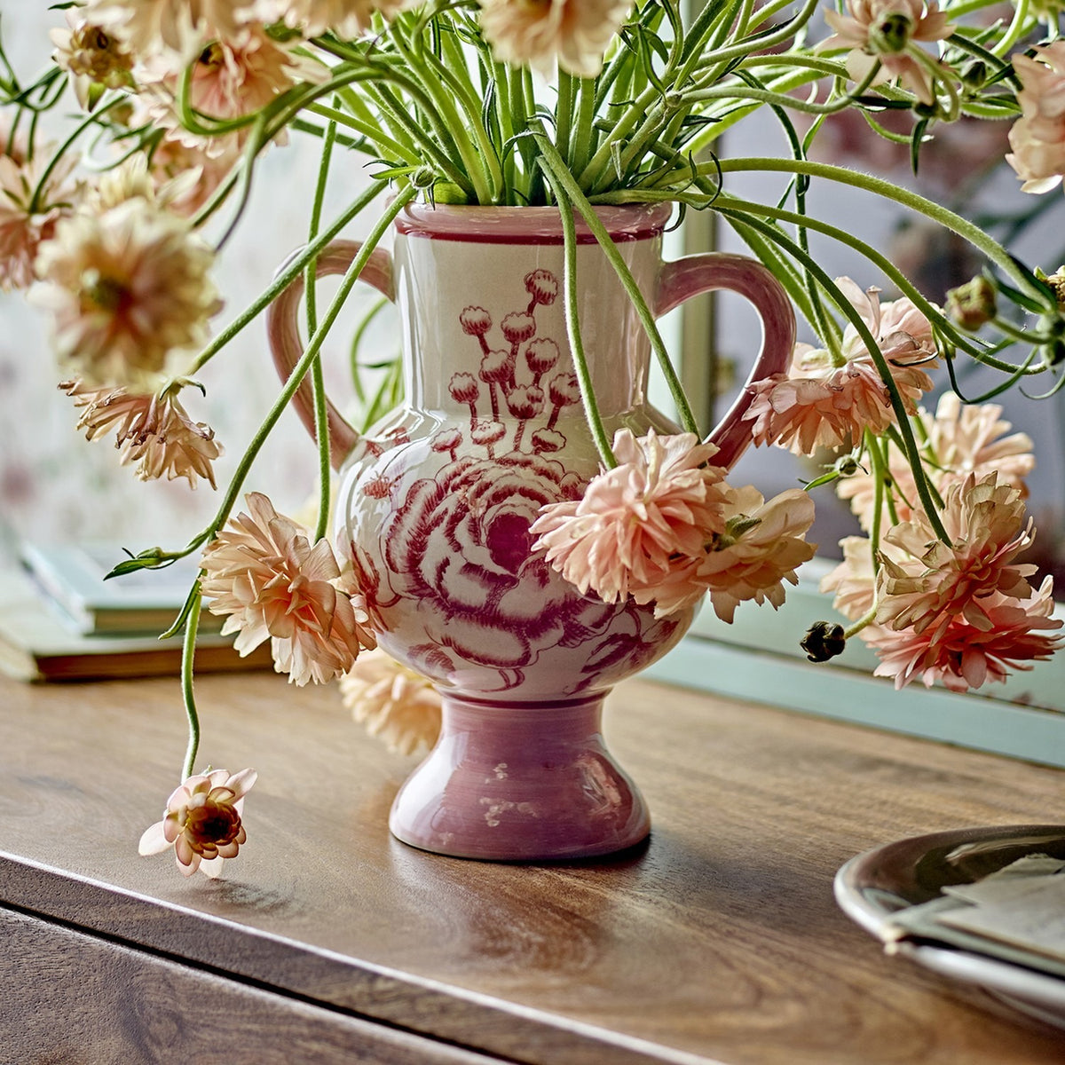 Alea Floral Stoneware Vase 21cm in pink with hand-painted rose design, loop handles and pedestal foot, holding pink blooms on a wooden table.