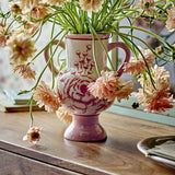 Alea Floral Stoneware Vase 21cm in pink with hand-painted rose design, loop handles and pedestal foot, holding pink blooms on a wooden table.