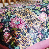 Lester Cotton Cushion in Multi, a rectangular fabric cushion with a dense printed pattern of stylised tigers, blooms and leaves in pink, gold and teal, finished with a pink fabric border.
