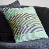 Isnel Green Striped Cushion in multicoloured horizontal stripes of green, blue and grey, woven fabric cover, shown resting on a dark grey sofa.