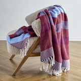 Isnel Red Striped Throw in multicoloured burgundy and blue stripes with ribbed texture and knotted fringe, draped over a cream bouclé chair.