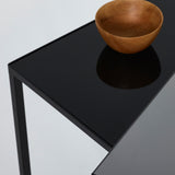 Close-up of the dark mirrored glass top with a turned wooden bowl resting on it, the underside of the bowl caught in the reflection.