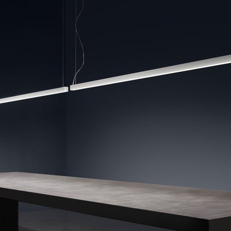 Brooklyn Line Aluminium Linear LED Pendant Light in white, a slim 102cm bar suspended on thin cables above a grey tabletop in a dark-toned room.