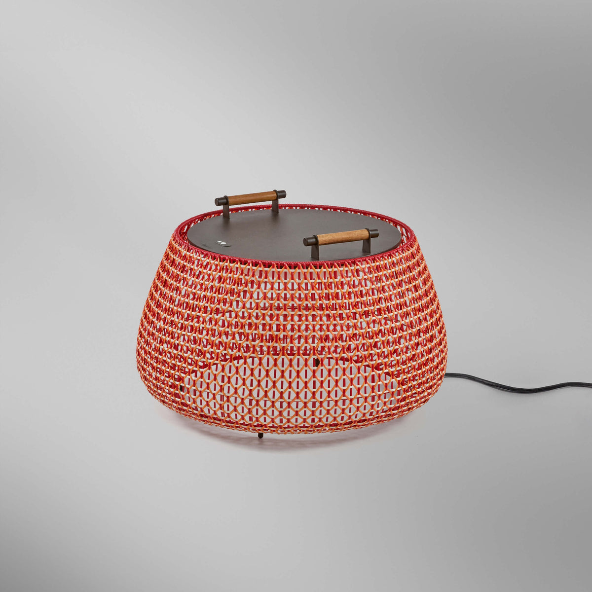 Nans Bag/38 Wood LED outdoor floor lamp, round woven basket-style shade in red with orange and beige lattice, flat dark top with wood handles, on a plain grey background.