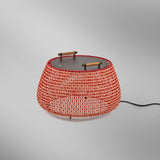Nans Bag/38 Wood LED outdoor floor lamp, round woven basket-style shade in red with orange and beige lattice, flat dark top with wood handles, on a plain grey background.