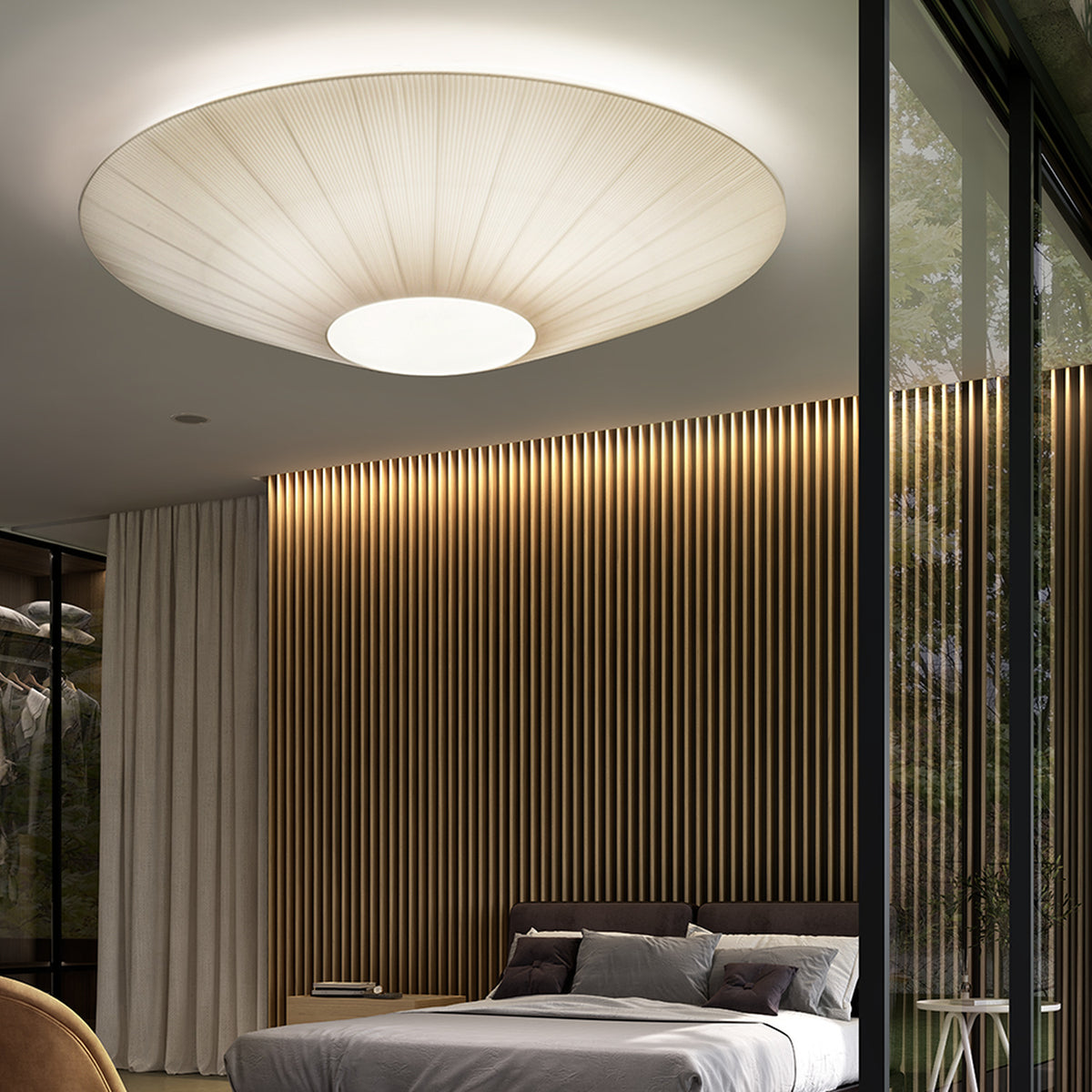 Siam 200 Ribbon Ceiling Light in cream, a wide pleated cone shade with central white disc, shown lit above a bed in a modern bedroom.