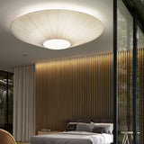 Siam 200 Ribbon Ceiling Light in cream, a wide pleated cone shade with central white disc, shown lit above a bed in a modern bedroom.