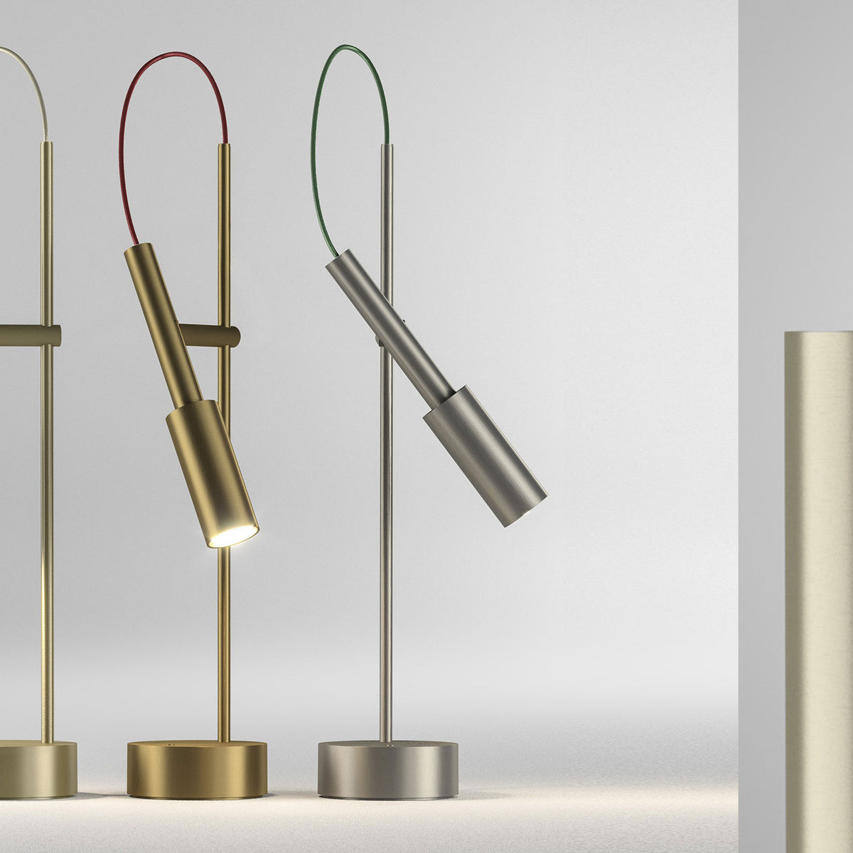 Tubino Aluminium LED Table Lamp in brushed titanium finish, slim stem with angled cylindrical head and looped green cable, round base, shown beside brass versions on a light grey background.