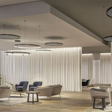 Arena Acoustic Disc LED Pendant Light in black, large flat disc pendants with slim rings and grey acoustic panels, suspended in a modern lounge above sofas and curtained walls.