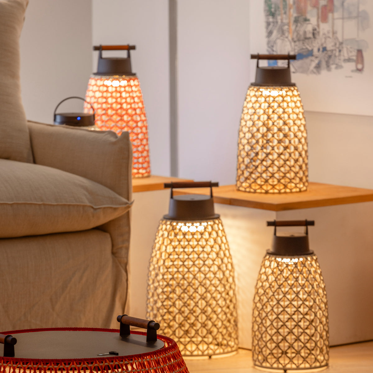 Nans Portable M/41 LED outdoor table lamps with woven lattice shades and wooden carry handles, glowing warm white on a wooden side table and floor in a living room setting.