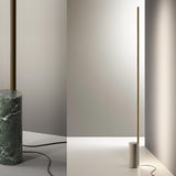 Hilow Line Alps Green Marble Linear Floor Lamp with slim brushed brass LED rod and round green marble base, shown beside a similar lamp on a travertine base.