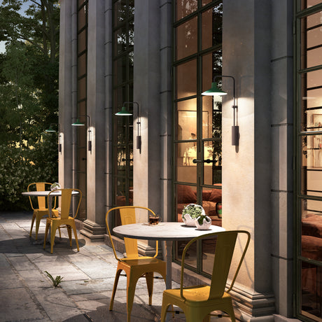 Platet A/01 outdoor wall lights with green shades on slim black arms, mounted along a columned building exterior above an outdoor dining terrace.