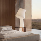Big Brother 3 Light Fabric Floor Lamp in white, tall tapering base with tilted drum shade, shown bedside in a modern room with woven screen and glass shelf accent.