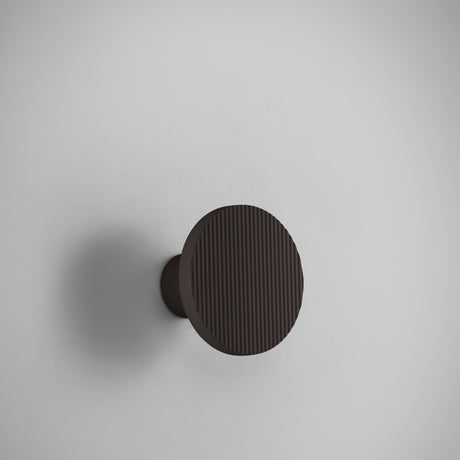 Arid A/01 round LED wall light in Textured Black aluminium, a fluted disc on a short stem projecting from the wall, shown against a plain light grey background.