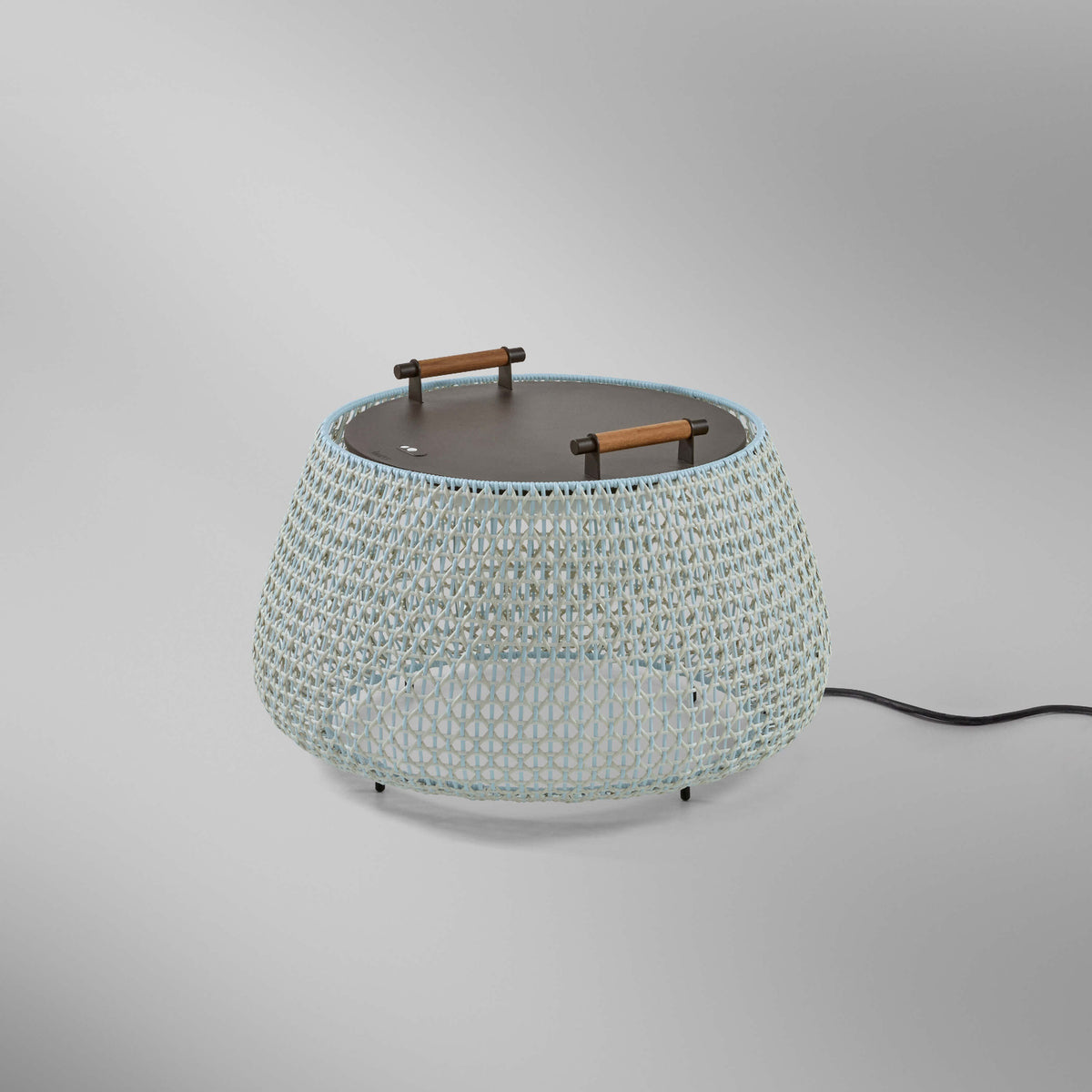 Nans Bag/38 Wood LED outdoor floor lamp with a wide woven beige shade, flat dark top, and two teak carry handles, shown on a plain grey background.