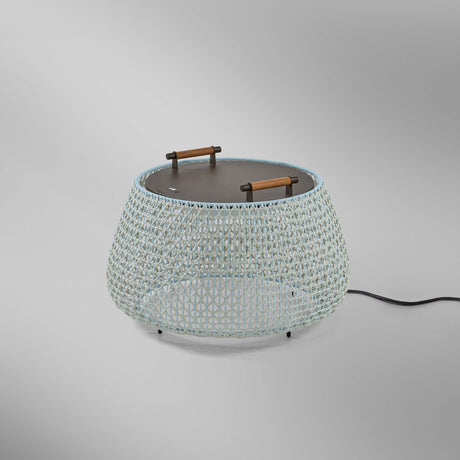 Nans Bag/38 Wood LED outdoor floor lamp with a wide woven beige shade, flat dark top, and two teak carry handles, shown on a plain grey background.