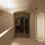 BIMU SV150 Metal Linear LED Pendant Light in black, shown as a slim suspended bar in a hallway with arched doorway and mirrored panels.